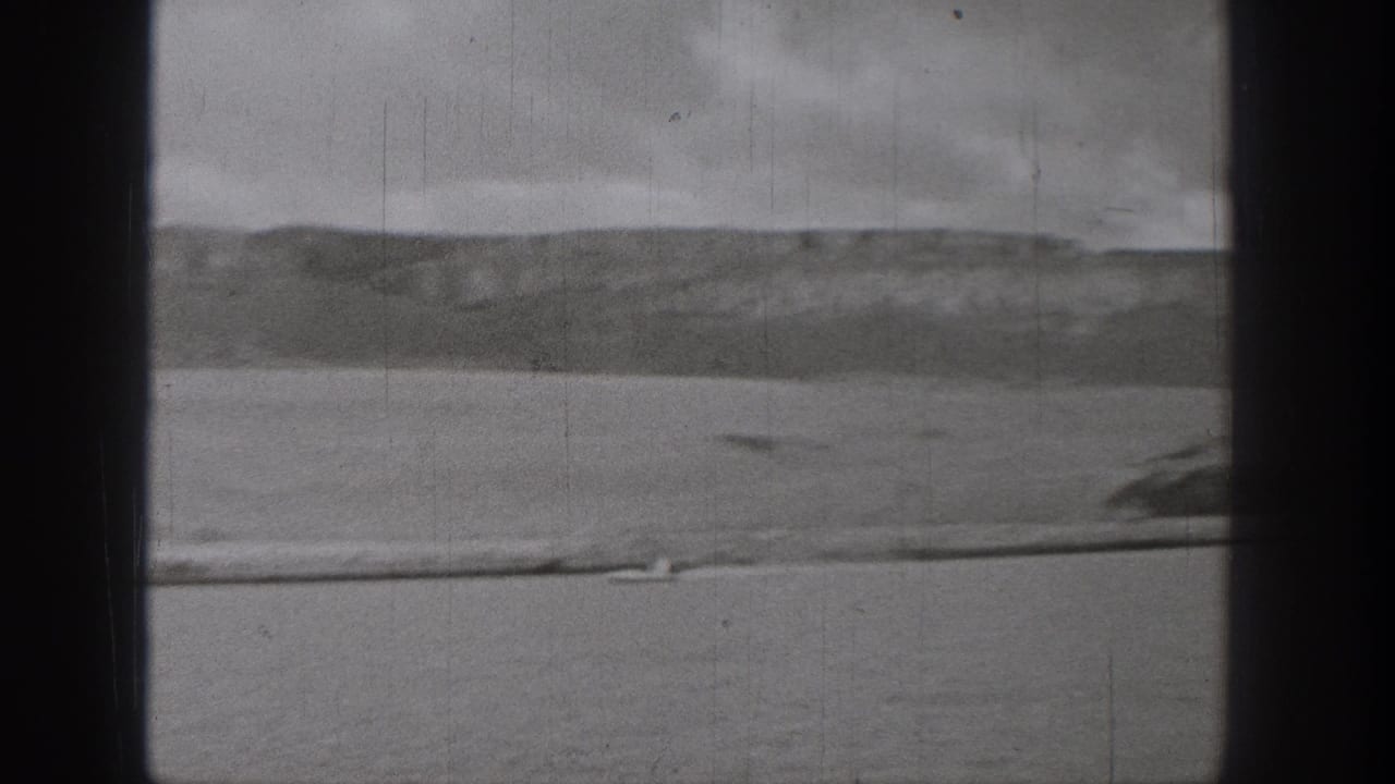 Grainy 1938 Washington 8mm frame with open lake water, distant hills, overcast sky, and a small boat near the foreground edge.