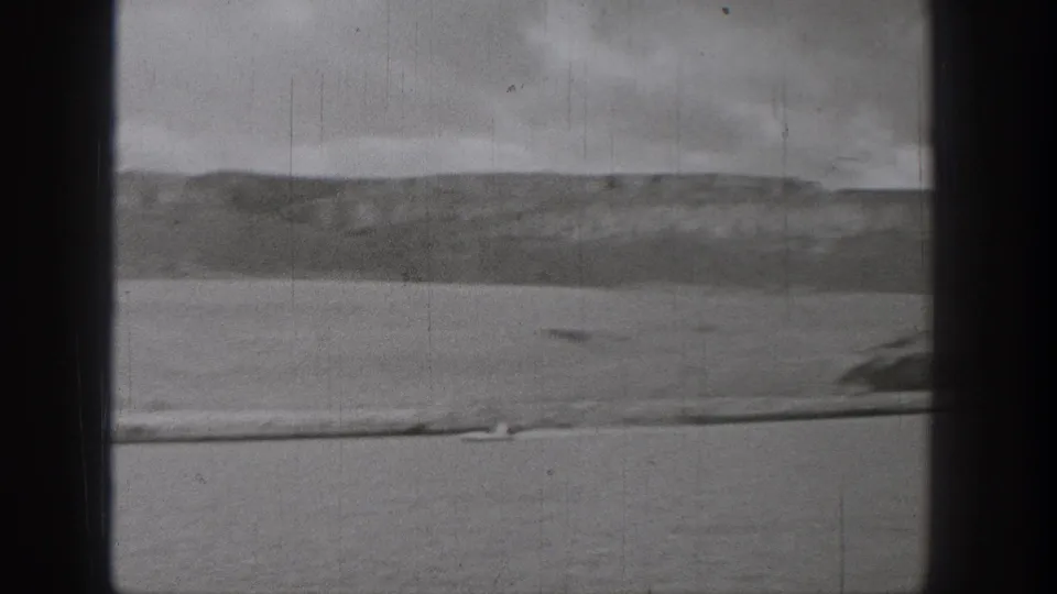 Grainy 1938 Washington 8mm frame with open lake water, distant hills, overcast sky, and a small boat near the foreground edge.