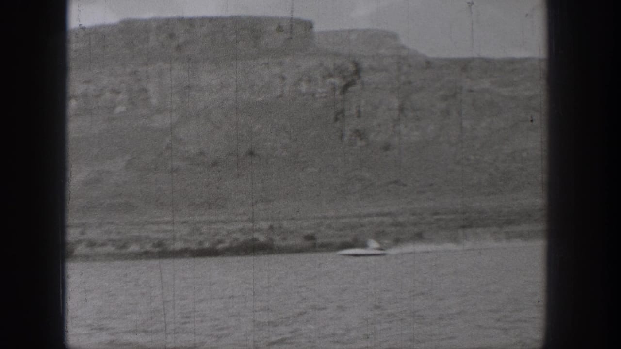 A small speedboat crosses the water near the shoreline below rugged Washington bluffs in grainy 1938 home-movie footage.