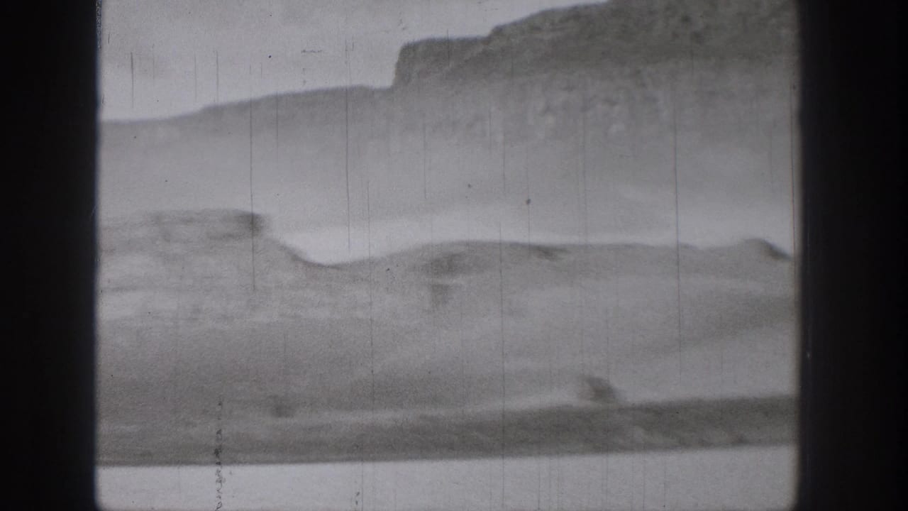 The speedboat leaves a pale wake across the water, with mesa-like bluffs softened by motion and 8mm film texture.