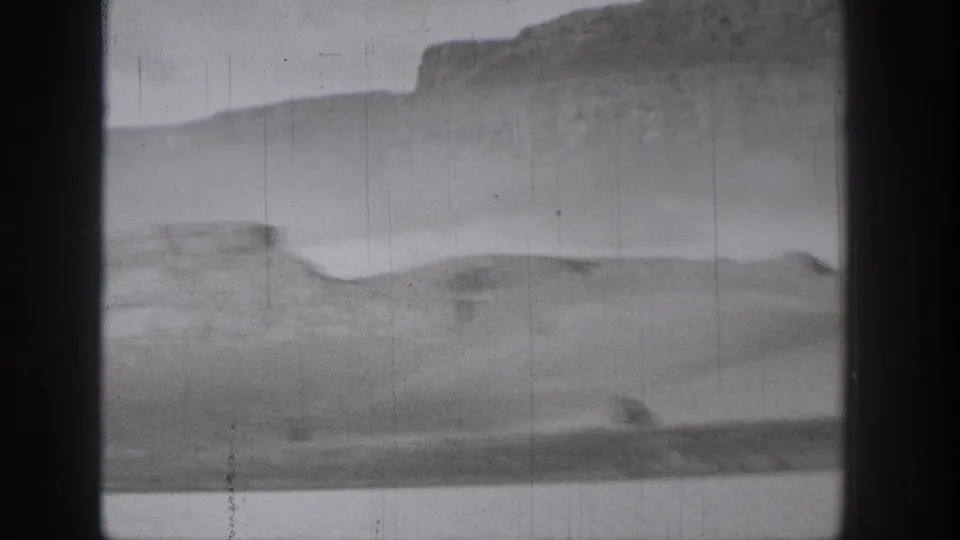 The speedboat leaves a pale wake across the water, with mesa-like bluffs softened by motion and 8mm film texture.