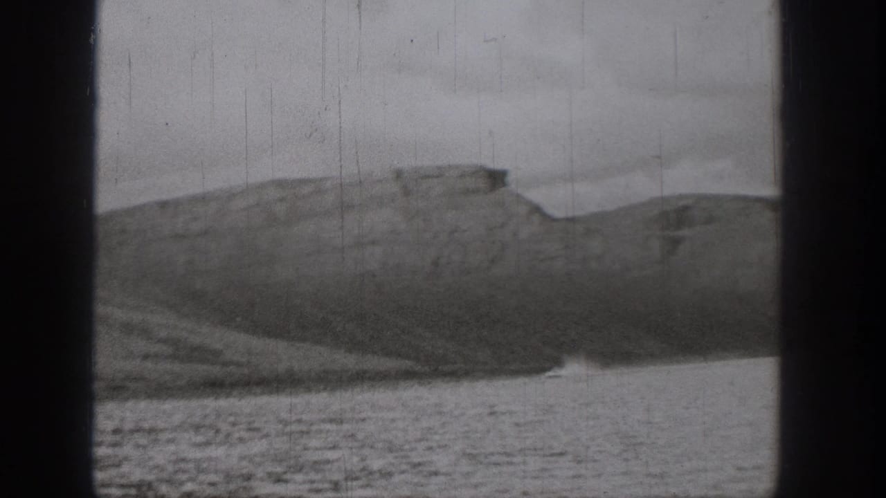 A wide 1938 Washington home-movie view shows wake on the water in front of dry, mesa-like bluffs and a dark film border.