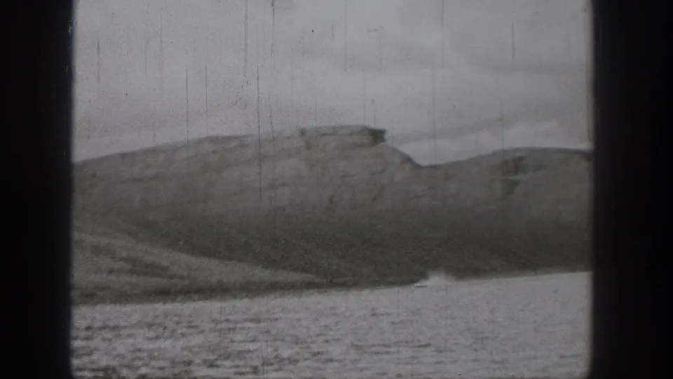 A wide 1938 Washington home-movie view shows wake on the water in front of dry, mesa-like bluffs and a dark film border.