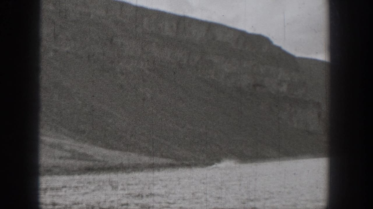 1938 Washington 8mm frame showing a rocky slope and rippled water viewed through a dark window frame.