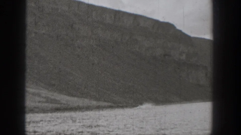 1938 Washington 8mm frame showing a rocky slope and rippled water viewed through a dark window frame.