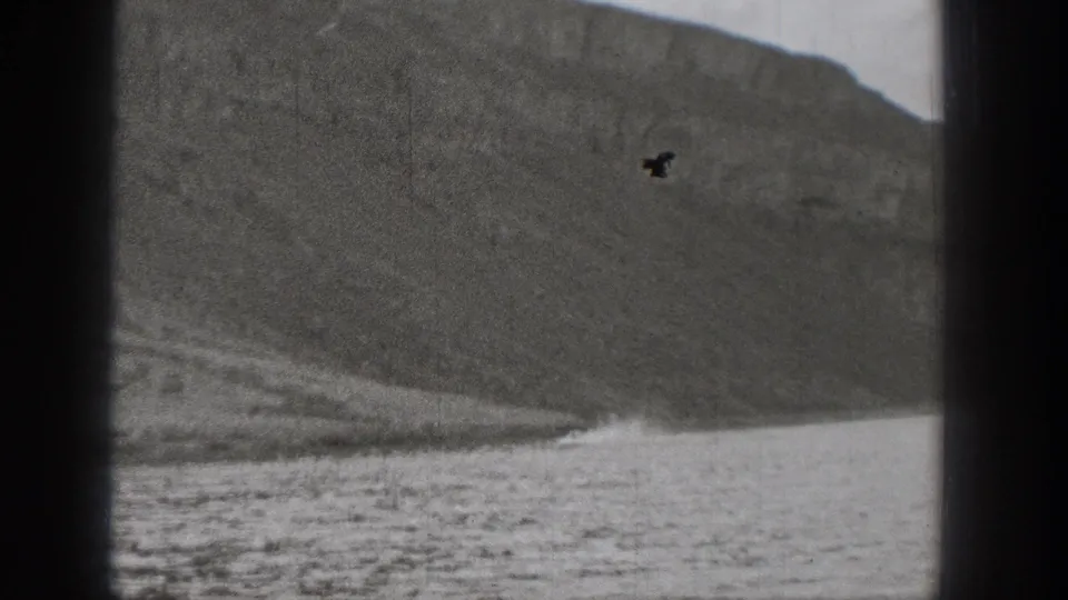 1938 Washington home-movie frame of a rocky waterside slope and calm water, partly blocked by window-frame edges.