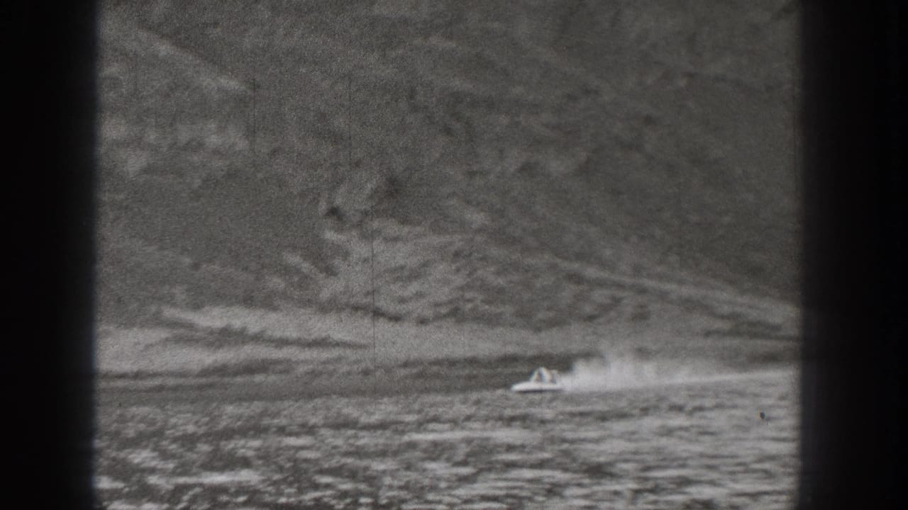1938 Washington 8mm frame with a small motorboat crossing a mountain-lined body of water and throwing a bright wake.