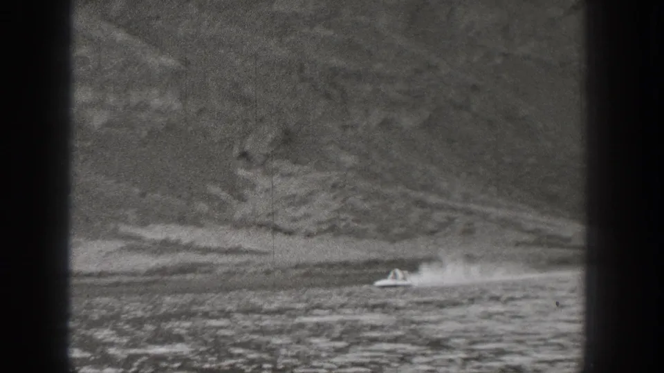 1938 Washington 8mm frame with a small motorboat crossing a mountain-lined body of water and throwing a bright wake.