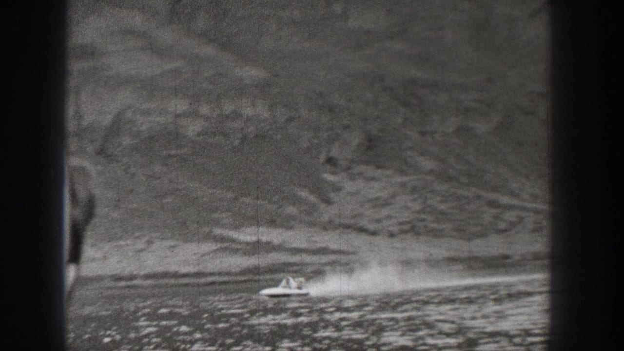 1938 Washington 8mm frame showing a small motorboat moving across lake water near a wooded mountain slope.