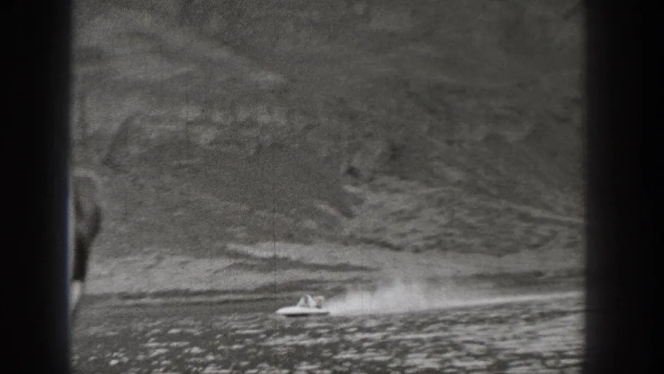 1938 Washington 8mm frame showing a small motorboat moving across lake water near a wooded mountain slope.