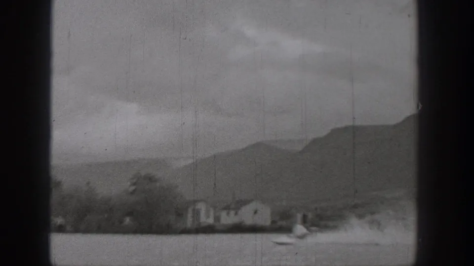 1938 Washington lake view with a small boat and wake near shoreline houses, trees, and low mountains.
