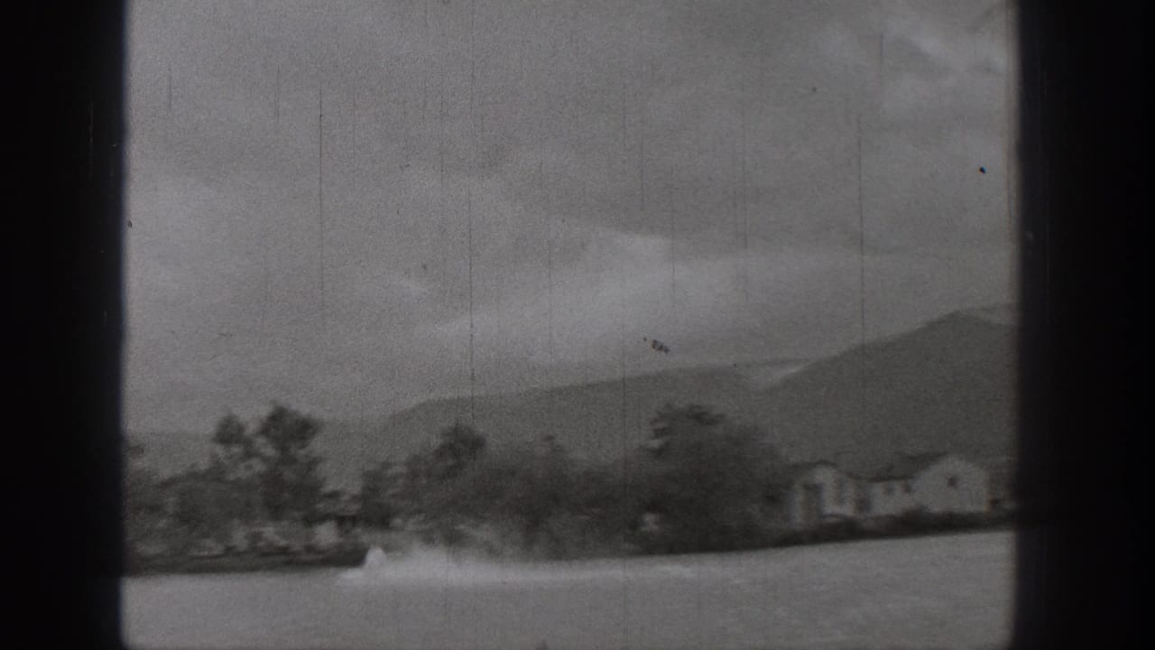 1938 Washington home-movie frame of lakeside houses and trees with a motorboat wake crossing the water.