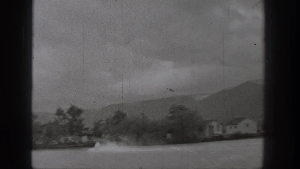 1938 Washington home-movie frame of lakeside houses and trees with a motorboat wake crossing the water.