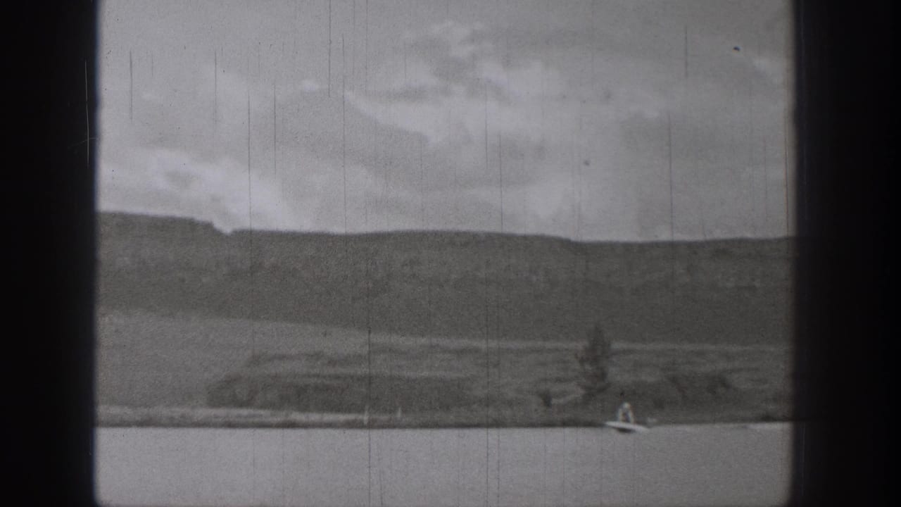 1938 Washington 8mm frame showing a small boat on open lake water below distant mountains and overcast sky.