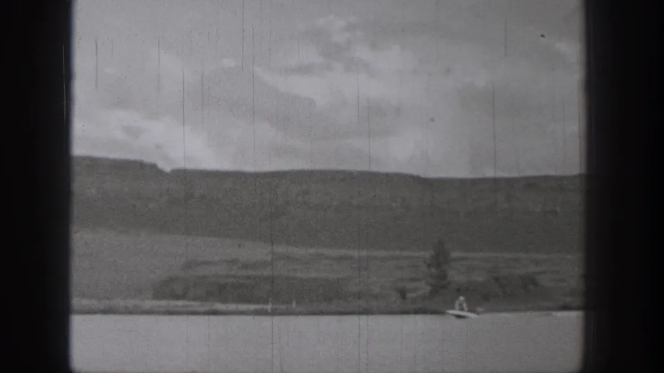 1938 Washington 8mm frame showing a small boat on open lake water below distant mountains and overcast sky.