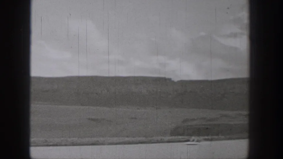 1938 Washington frame with a distant person riding a motorized surf-like device across the lake near a low shoreline.