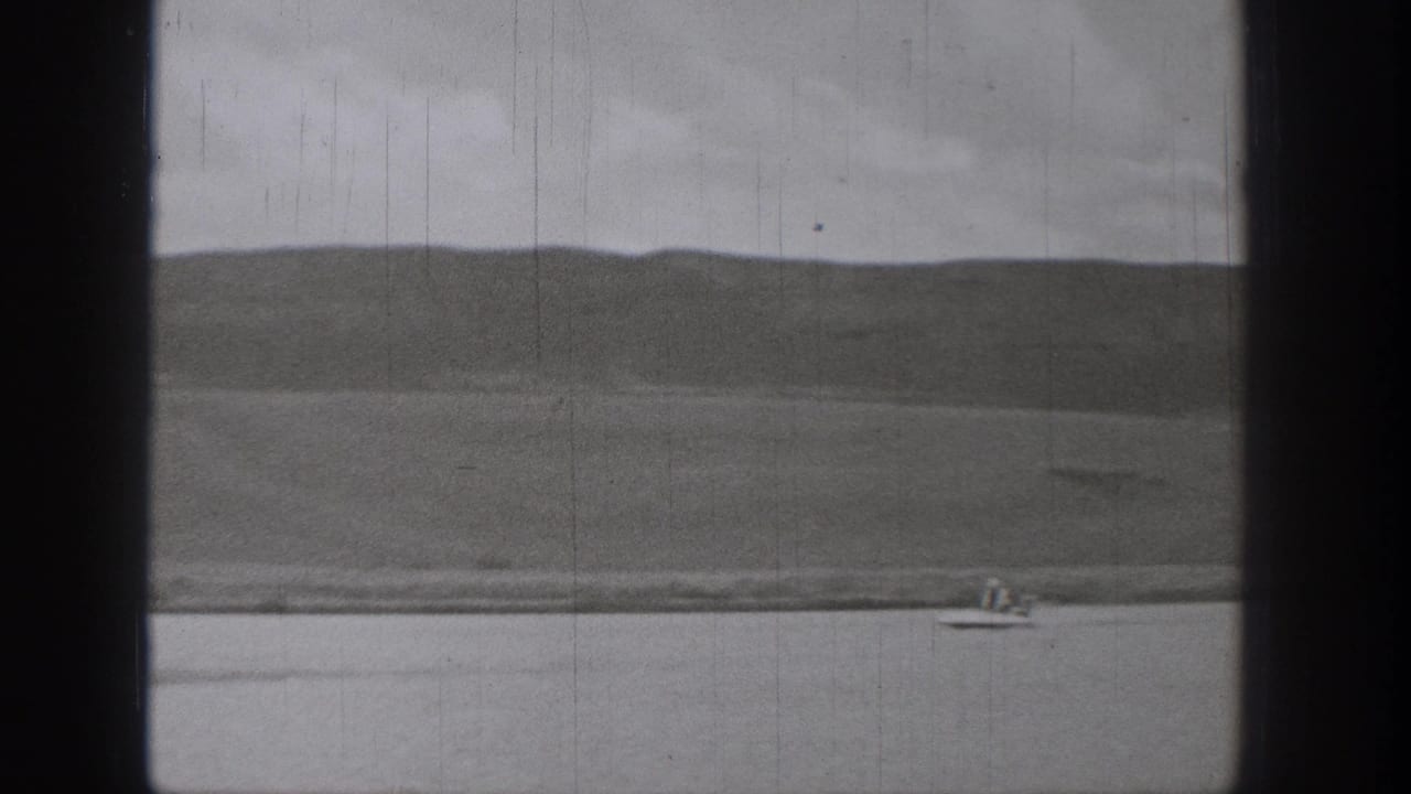 Archival 8mm frame from Washington in 1938 showing a distant rider on a motorized surf-like device against lake and hillside.
