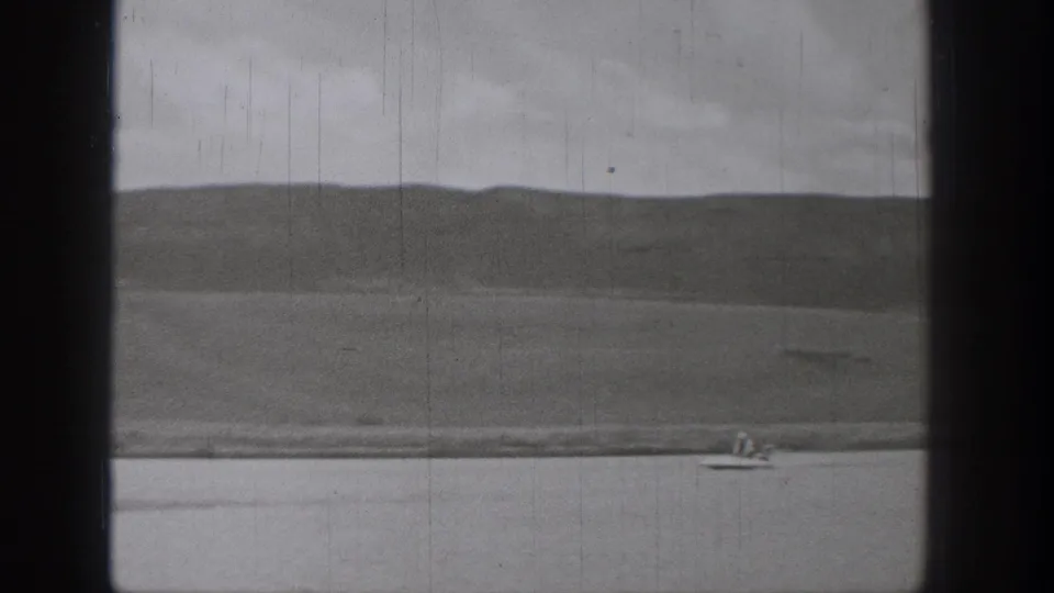 Archival 8mm frame from Washington in 1938 showing a distant rider on a motorized surf-like device against lake and hillside.