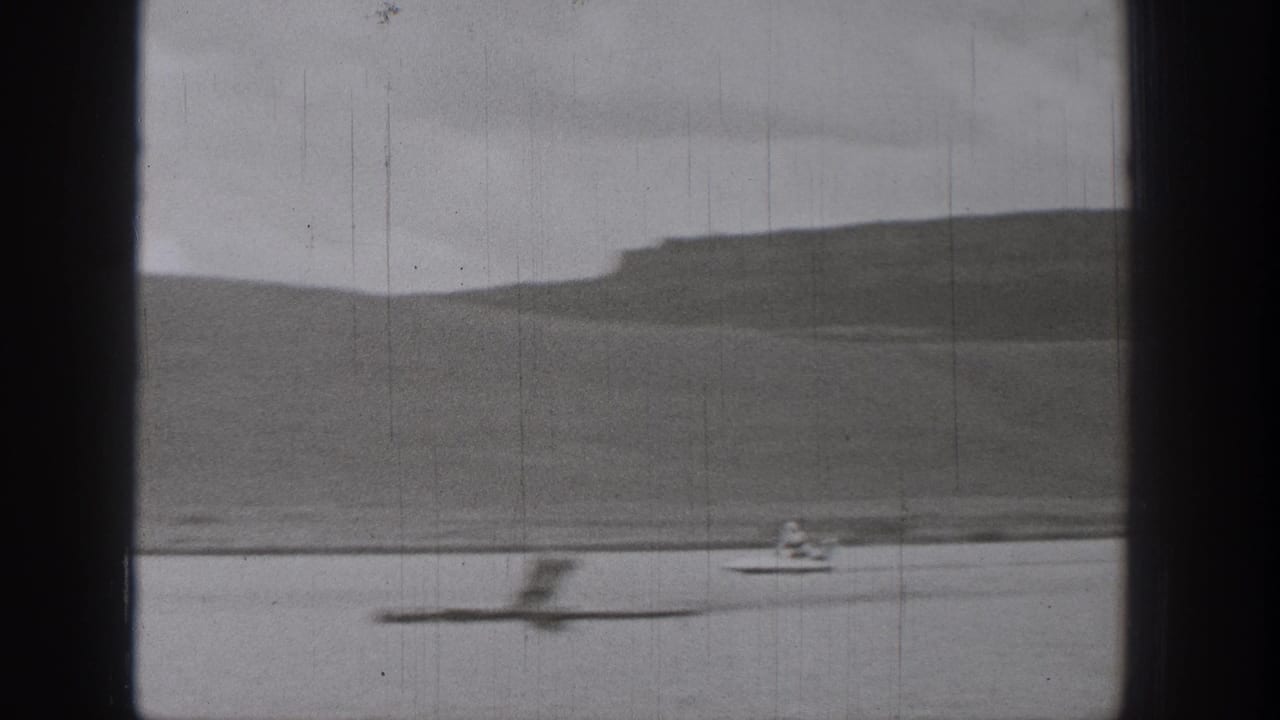 1938 Washington lake frame with a blurred object or wake in the foreground and a distant motorized surf-device rider near the far shore.
