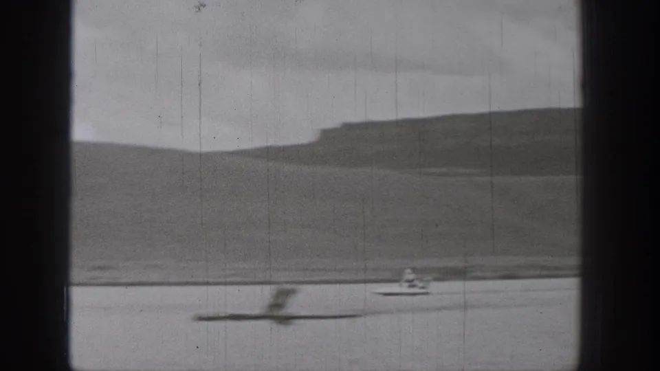 1938 Washington lake frame with a blurred object or wake in the foreground and a distant motorized surf-device rider near the far shore.