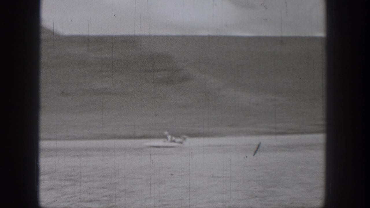 Distant small boat on open water with shoreline hills and visible film scratches.