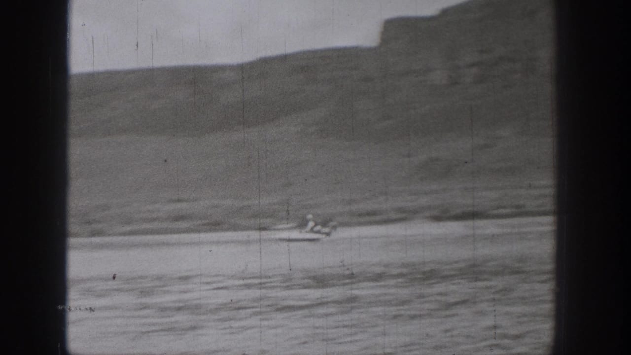 A small boat, possibly carrying a dog or small occupant, passes through a soft 8mm view of Washington water and hills.