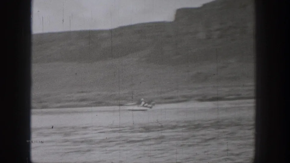 A small boat, possibly carrying a dog or small occupant, passes through a soft 8mm view of Washington water and hills.