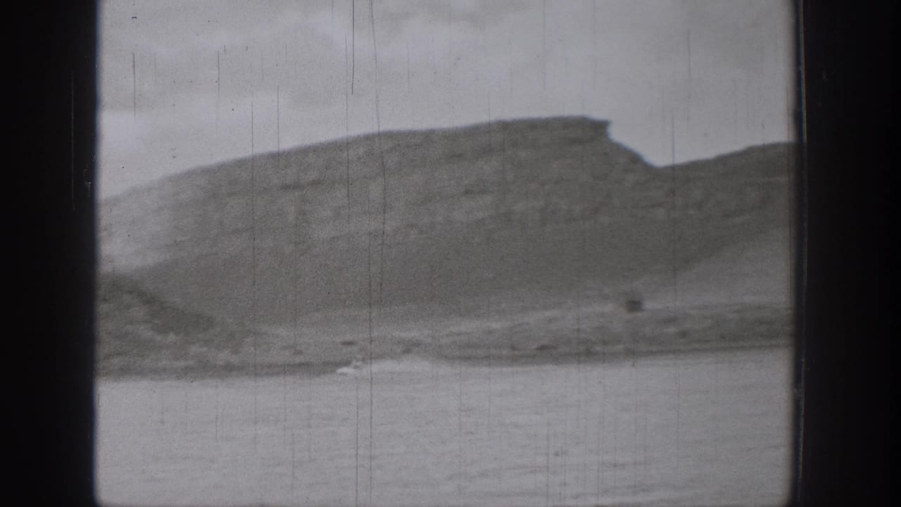 Distant cliff ridge and lake water with visible 8mm film scratches.