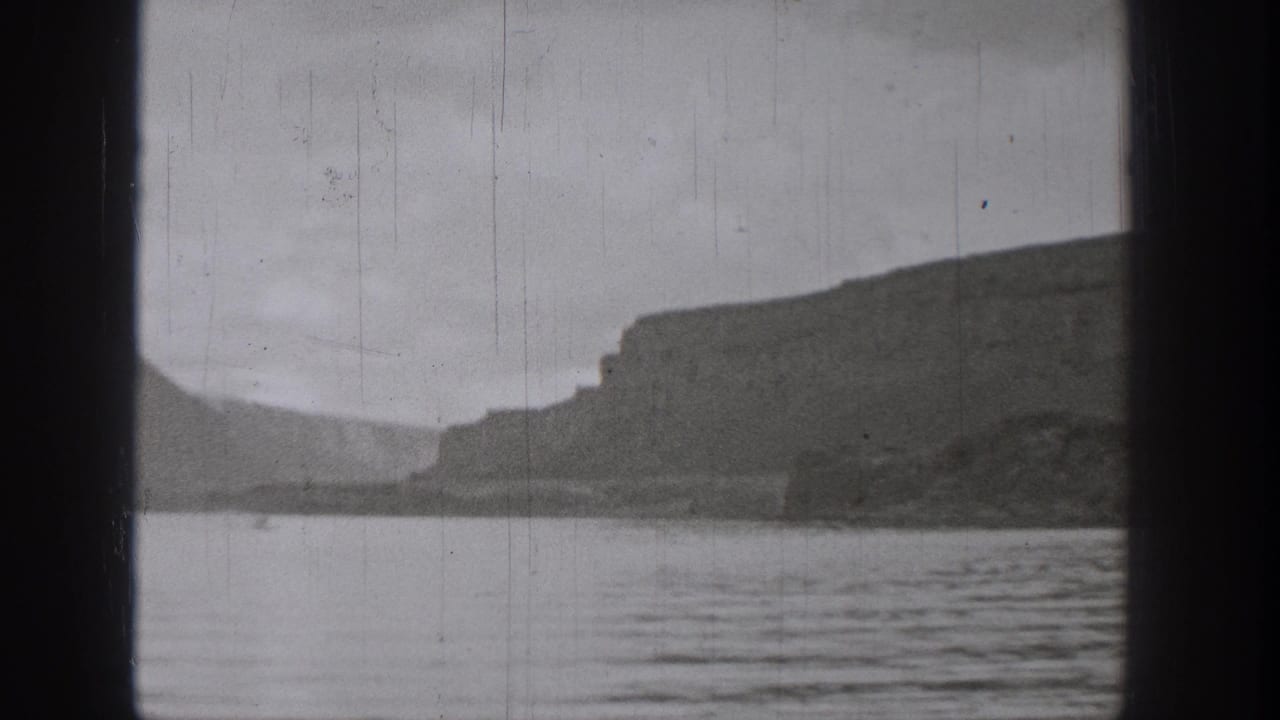 1938 Washington home-movie frame showing a rocky lakeshore and rippled water from a boat-like viewpoint.