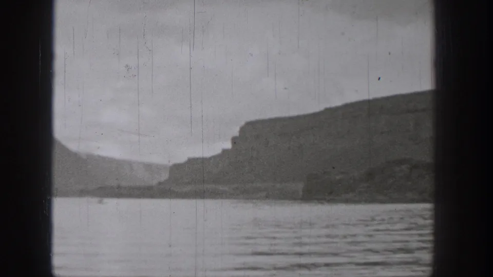 1938 Washington home-movie frame showing a rocky lakeshore and rippled water from a boat-like viewpoint.