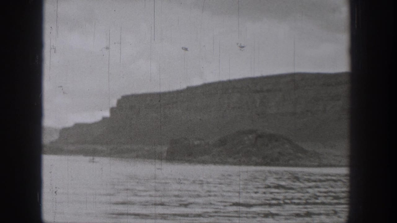Black-and-white 8mm frame of a Washington lake shoreline with cliffs, water ripples, and visible film wear.