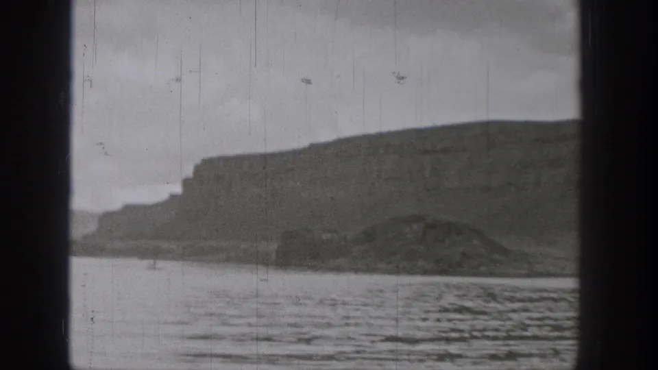 Black-and-white 8mm frame of a Washington lake shoreline with cliffs, water ripples, and visible film wear.