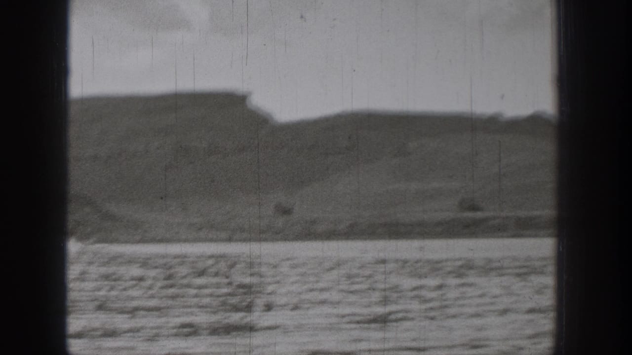 1938 Washington lake scene with low hills, distant shore, rippled foreground water, and scratched 8mm texture.