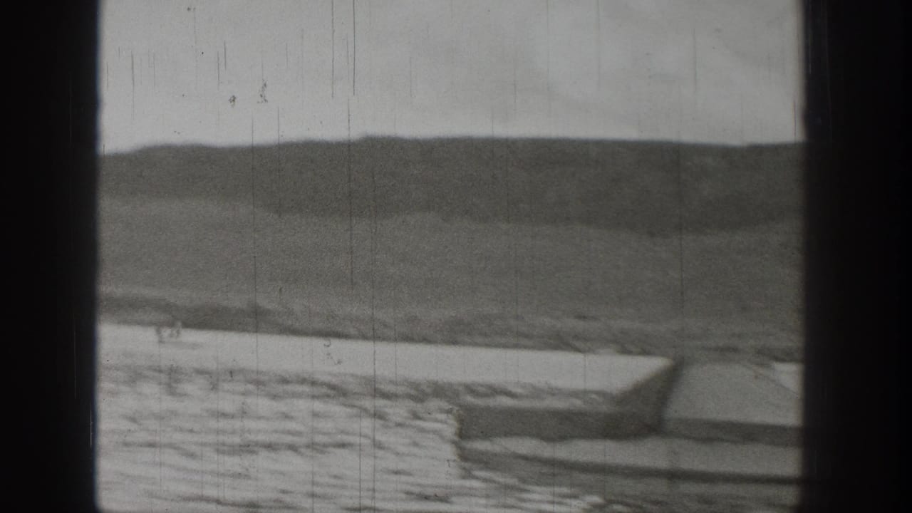 1938 Washington home-movie view of a small boat on a lake beneath rugged hills, partially obscured by dark window-frame borders.