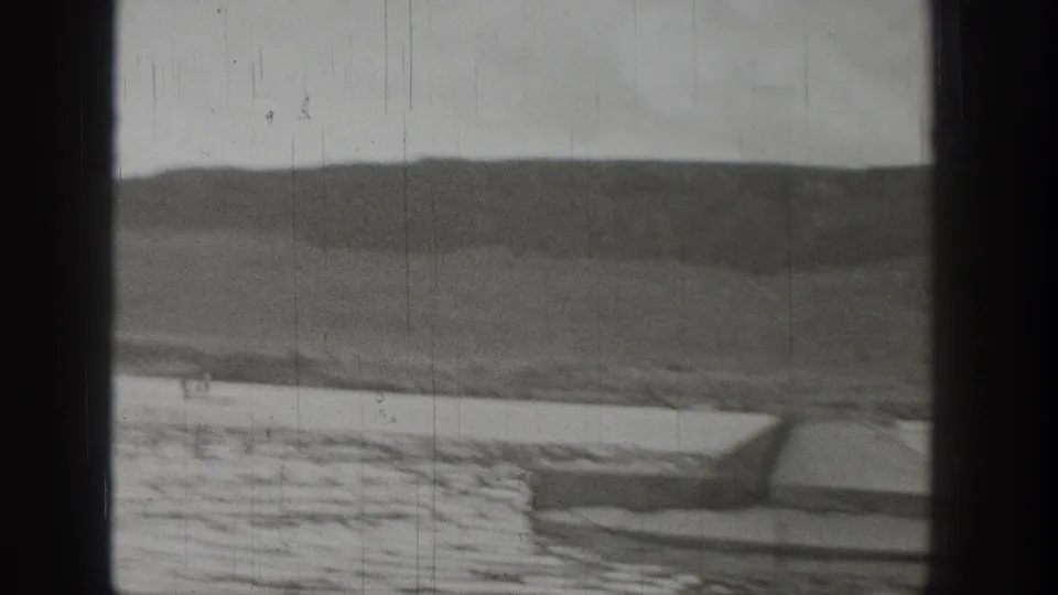 1938 Washington home-movie view of a small boat on a lake beneath rugged hills, partially obscured by dark window-frame borders.