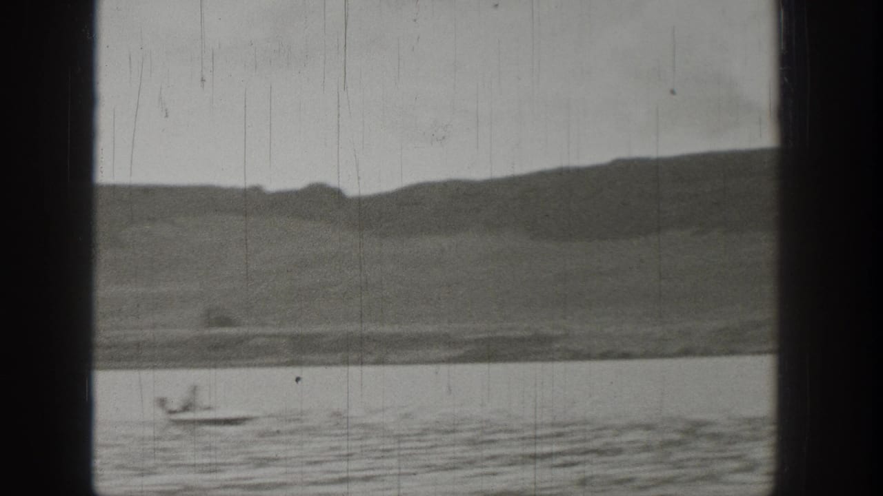 A small boat travels across a Washington lake, framed by rounded hills and the dark borders of the filmed window view.