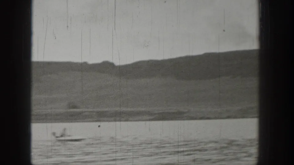 A small boat travels across a Washington lake, framed by rounded hills and the dark borders of the filmed window view.