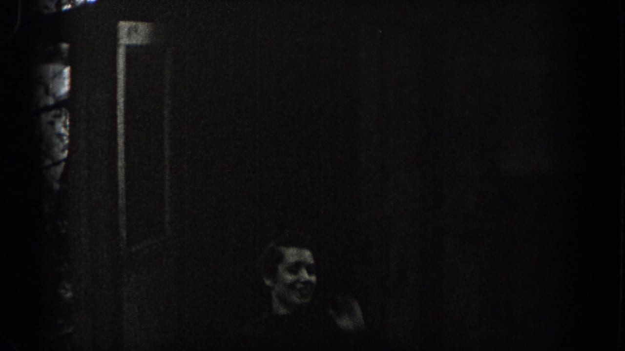 Washington 1938 home-movie frame showing a woman near a cottage doorway, her face faintly visible in low exposure.