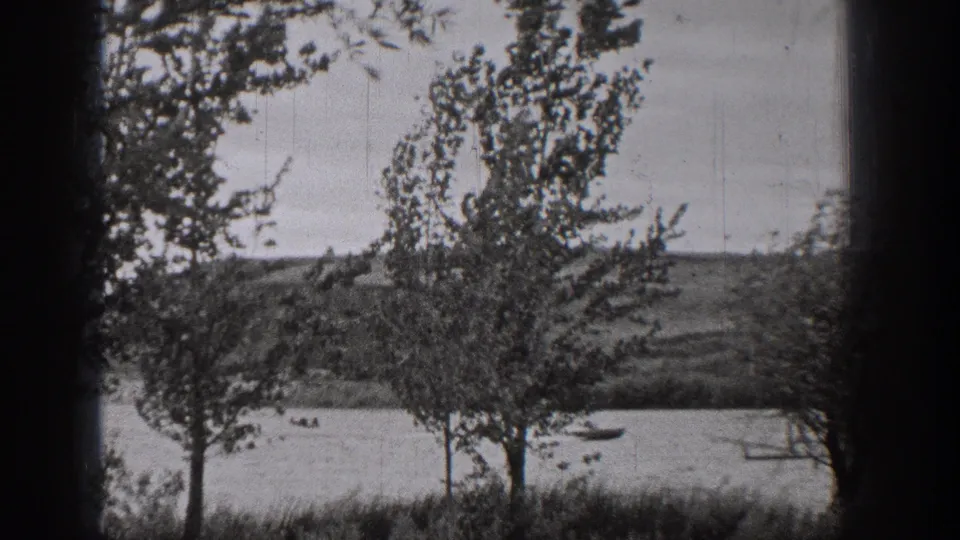 1938 Washington home-movie frame with trees in the foreground and small boats crossing a lake beyond.