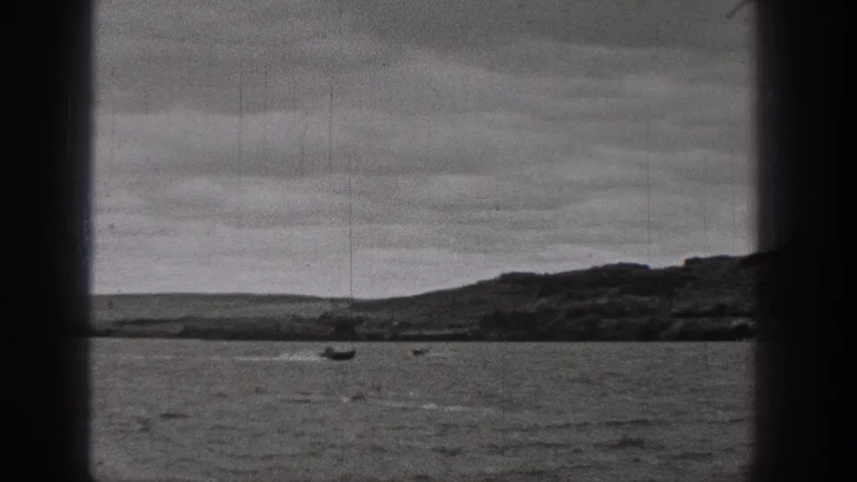 1938 Washington 8mm frame showing rippled lake water, small boats, low hills, and cloud cover.