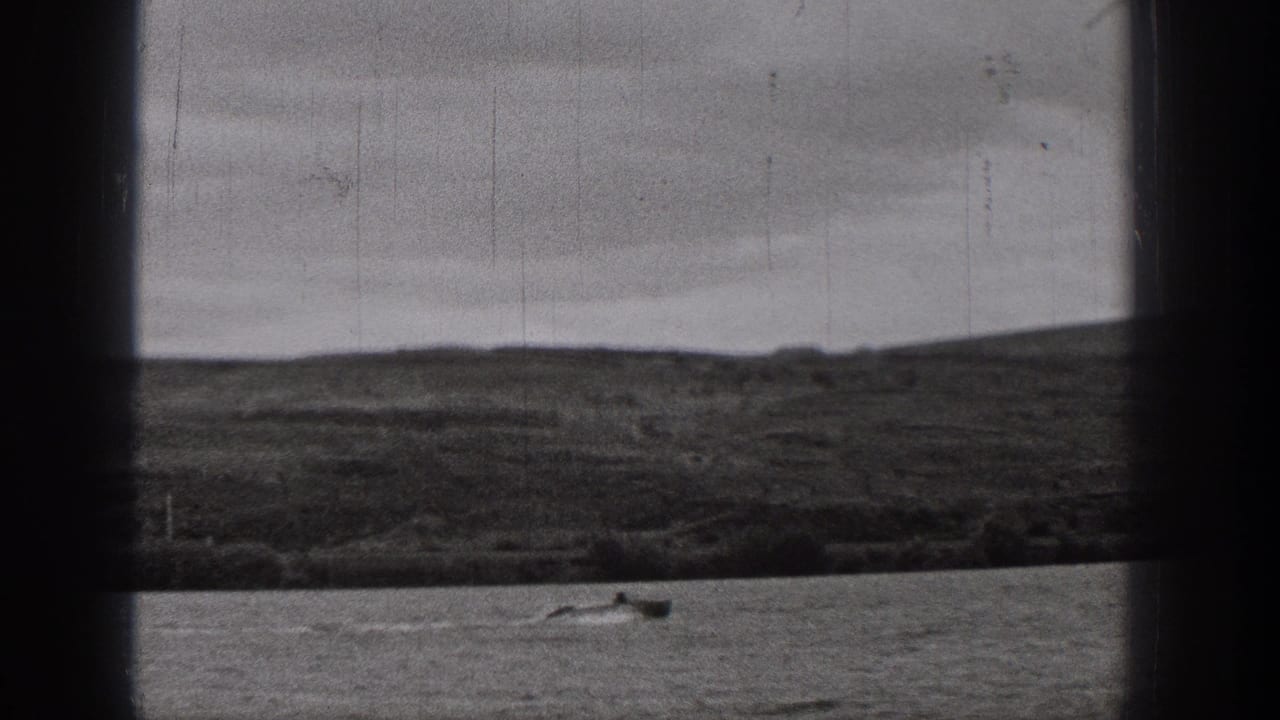 Small boat crossing water with low hills and cloudy sky beyond.