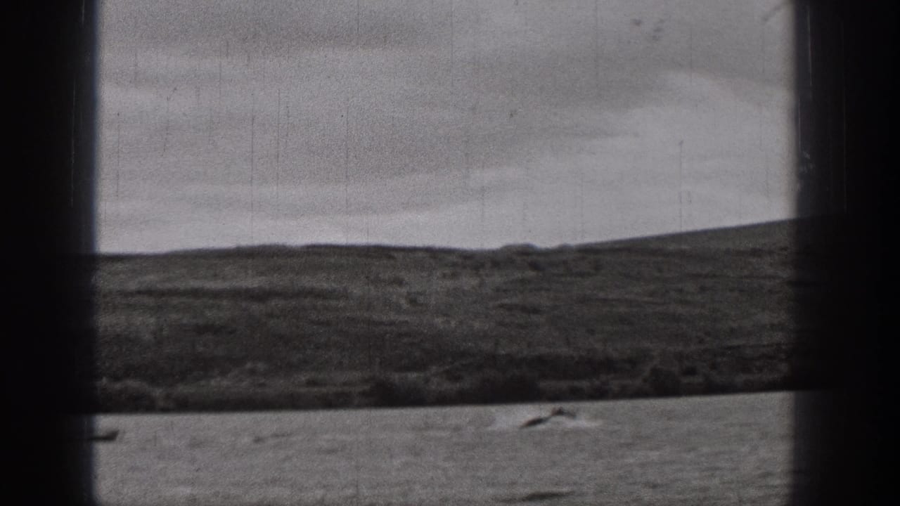 1938 Washington home-movie frame of a broad waterscape, distant rolling terrain, and a small boat near the lower edge.