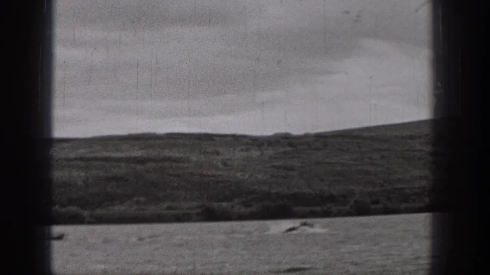 1938 Washington home-movie frame of a broad waterscape, distant rolling terrain, and a small boat near the lower edge.