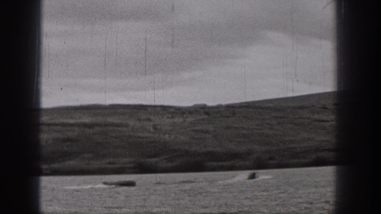 Late-1930s Washington 8mm frame showing cloudy sky, low hills, and small boats on a broad body of water.