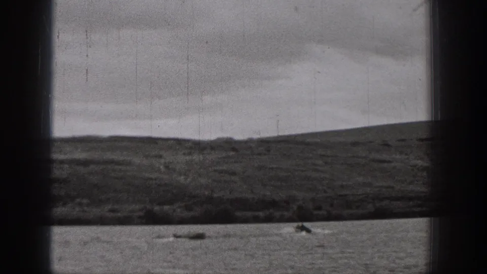 1938 Washington 8mm home-movie frame showing small boats on a lake with low hills and overcast sky in the background.