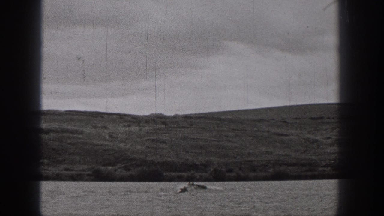 A small boat travels across the lake with low hills behind it.