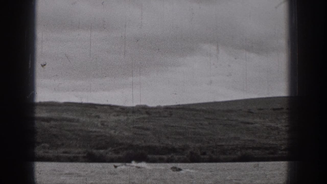 A small motorboat creates a visible wake on a lake, framed by dark 8mm borders and distant hills.