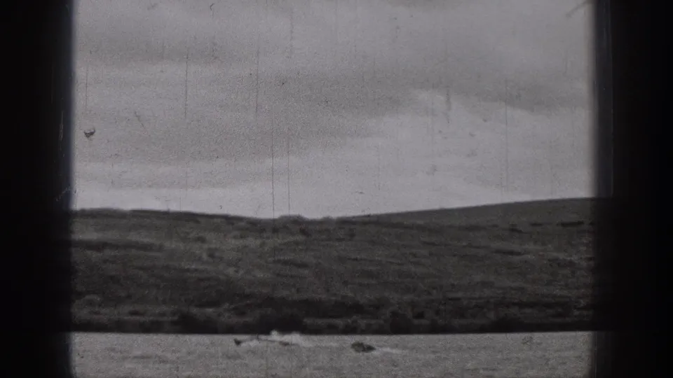 A small motorboat creates a visible wake on a lake, framed by dark 8mm borders and distant hills.