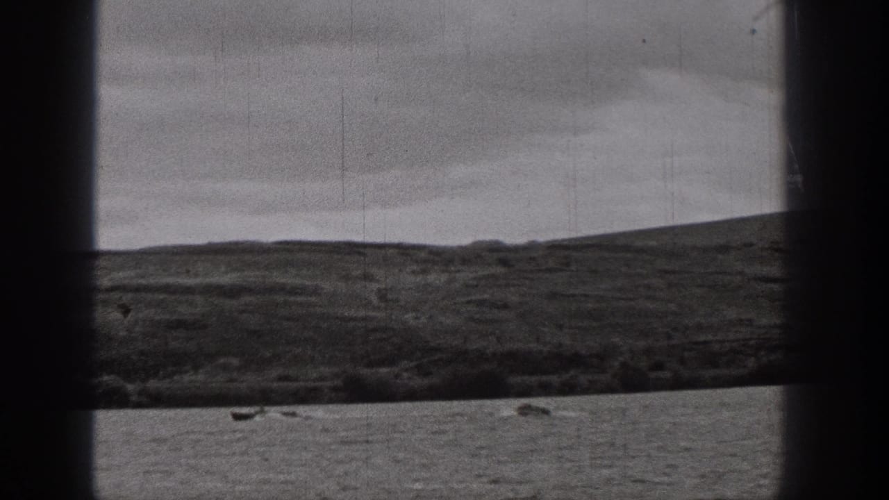 Distant lake boating appears in a 1938 Washington home-movie frame with hills, overcast sky, and visible film wear.