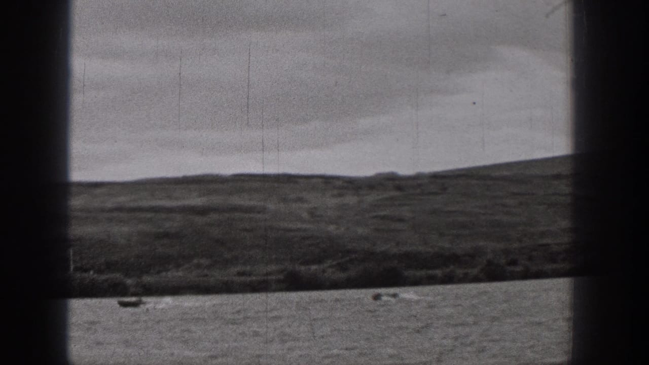 1938 Washington 8mm frame showing a small boat on rippled lake water below a low shoreline and overcast sky.